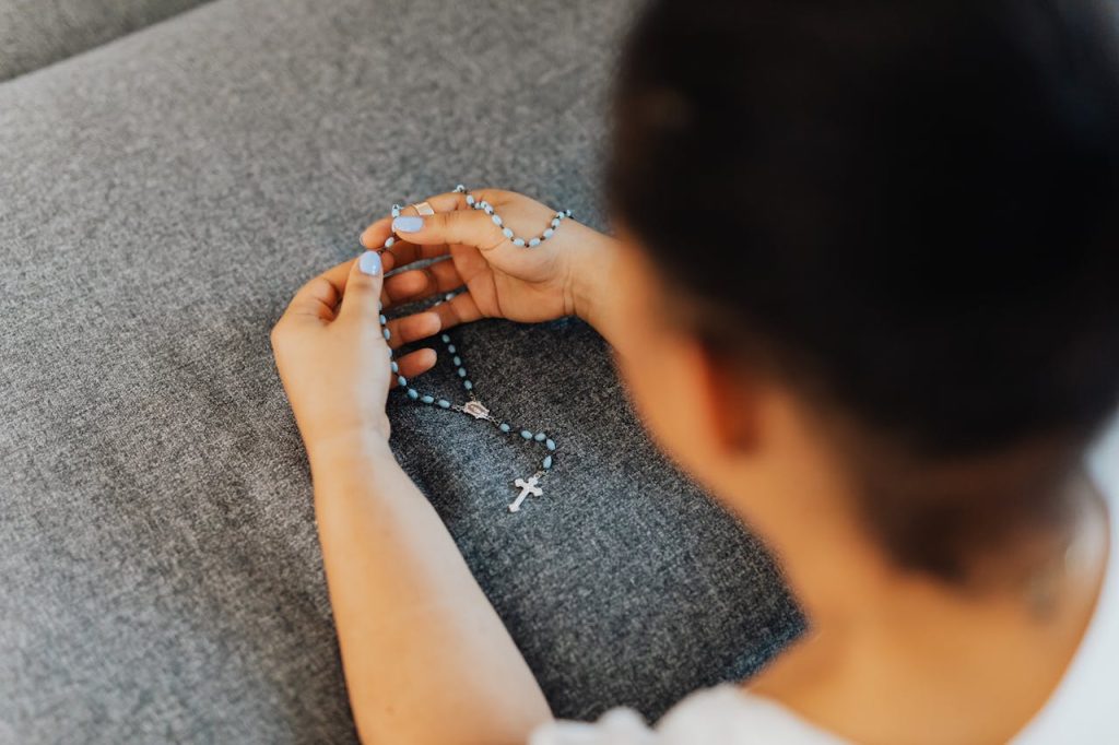 a-person-holding-a-rosary-5311306 A child holding blue rosary beads on a grey surface, symbolizing faith.
