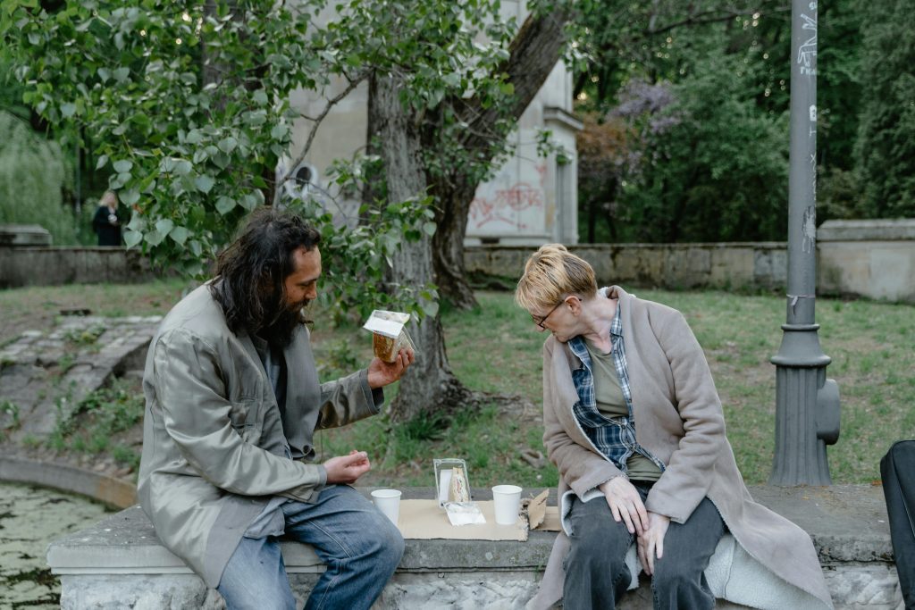 pexels-photo-8078370-8078370 Two individuals sitting in a park, engaged in conversation while sharing a meal on a stone bench.