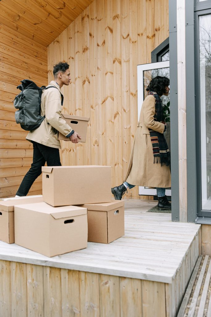 pexels-photo-8962202-8962202 A couple carries cardboard boxes into a modern wooden house, showcasing a new home move-in.